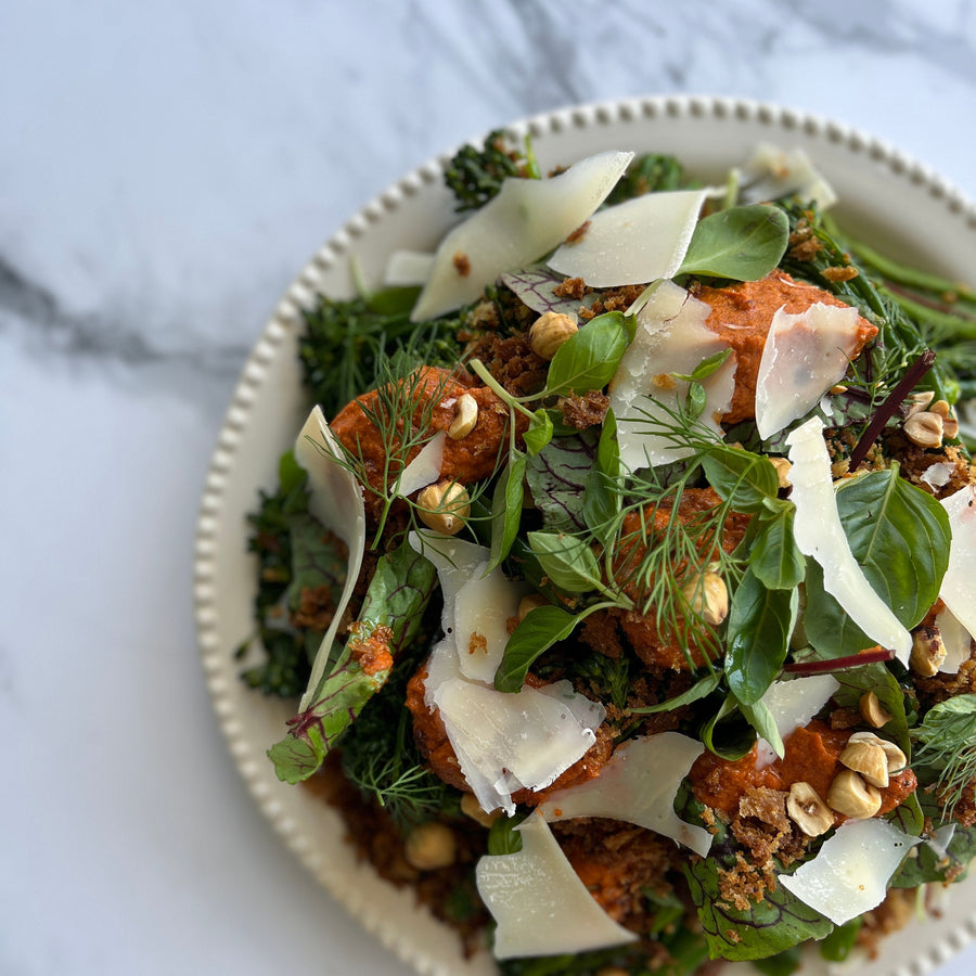 Salad with greens, romesco, hazelnuts and shaved cheese on a marble surface