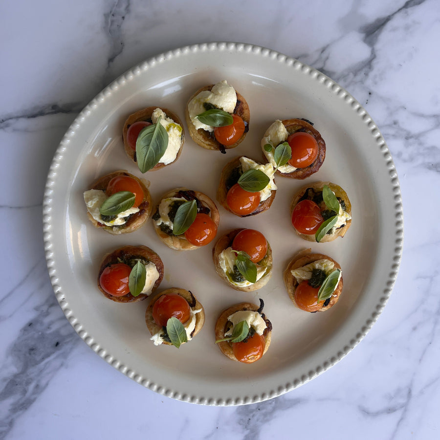 Platter of small appetizers with puff pastry confit cherry tomatoes basil pistou and fior di latte cheese on a marble surface