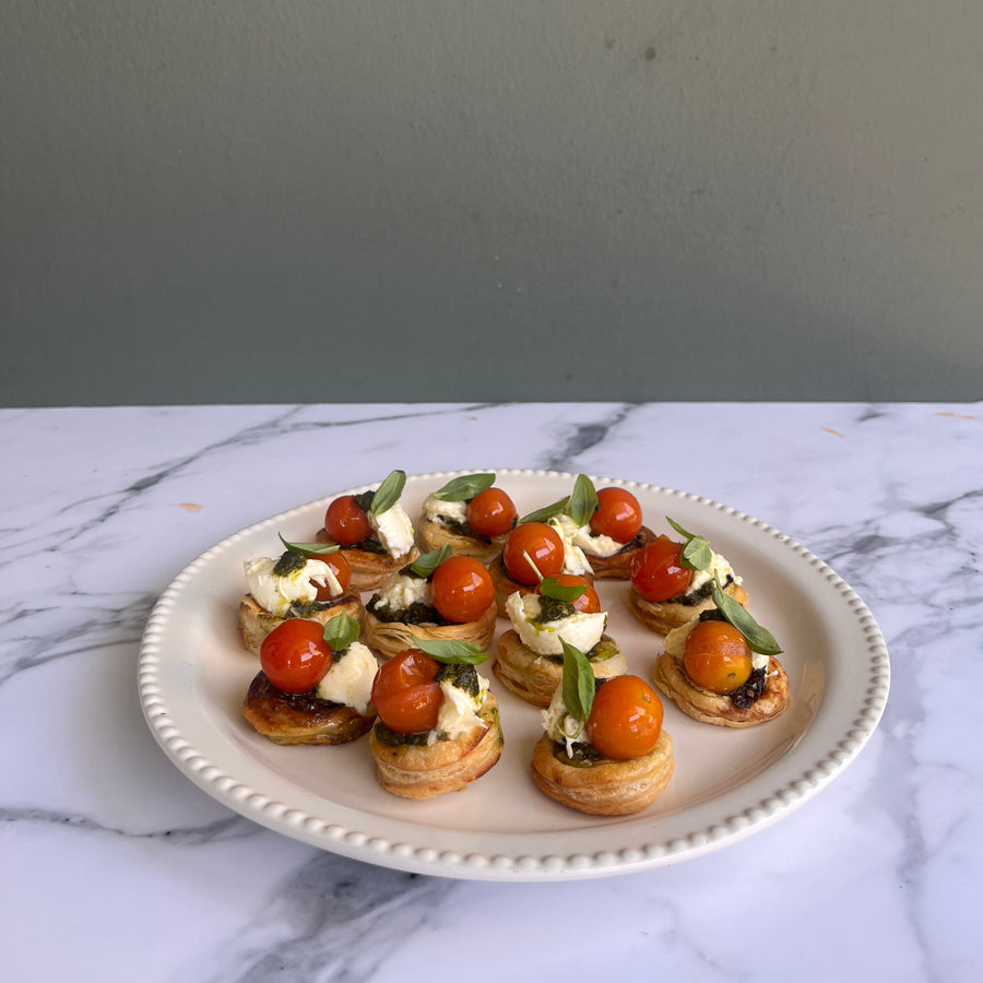 Platter of puff pastry canapes with cherry tomatoes, basil pistou an fior di latte on a marble surface