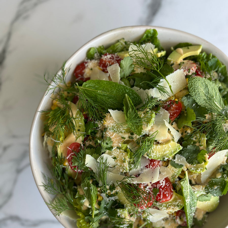 charred corn with avocado and baby gem and tomatoes in a white bowl on a marble surface