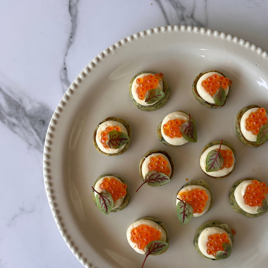 Elegant bite sized blinis topped with chive, horseradish crème fraîche and premium Yarra Valley salmon caviar on a marble surface