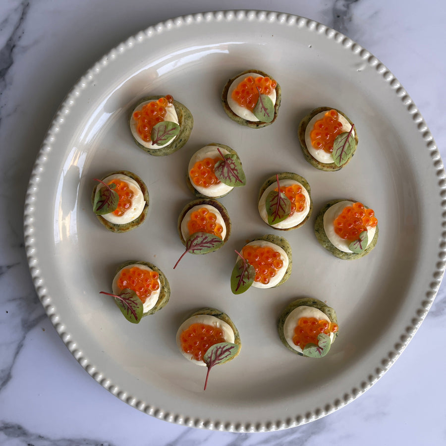 Platter of finger food blinis topped with chive, horseradish crème fraîche and premium Yarra
Valley salmon caviar on a marble surface