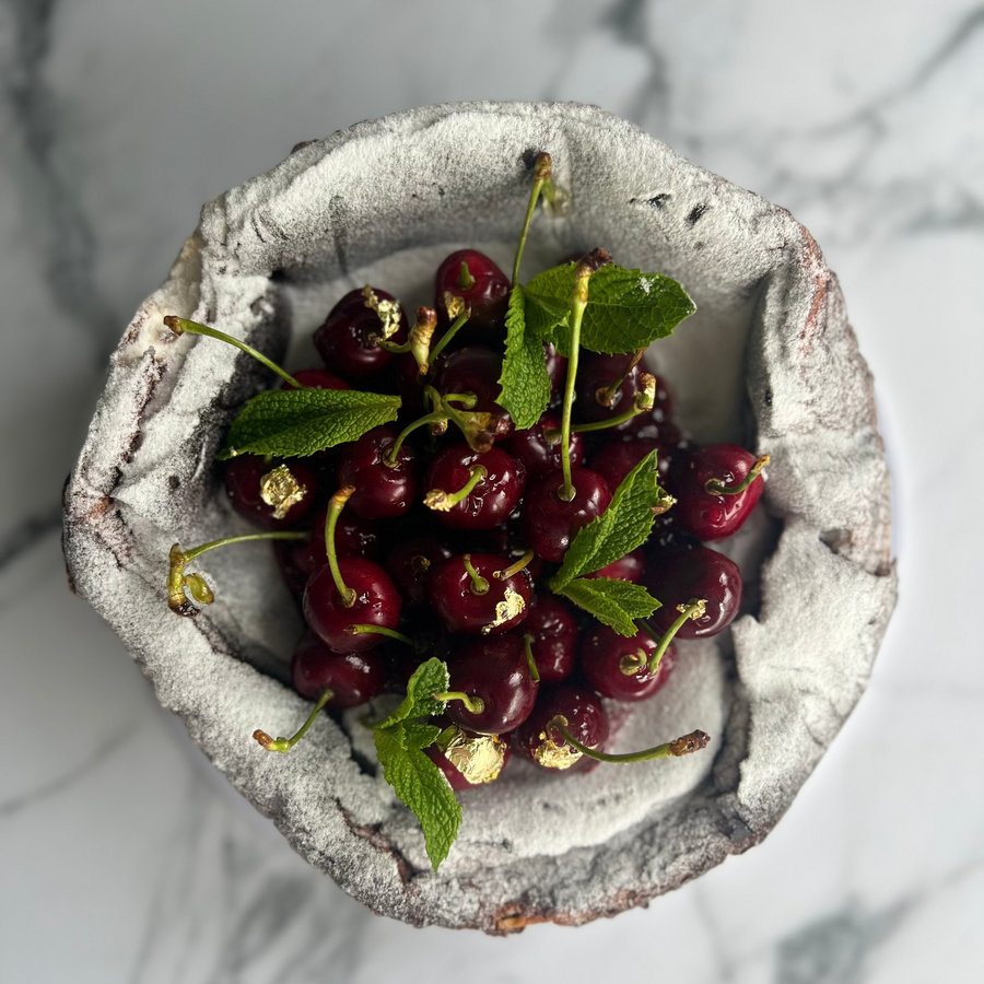 Vanilla Basque cheesecake pictured from the top with a  cherry jam and market fresh cherries to fill its center on a marble table