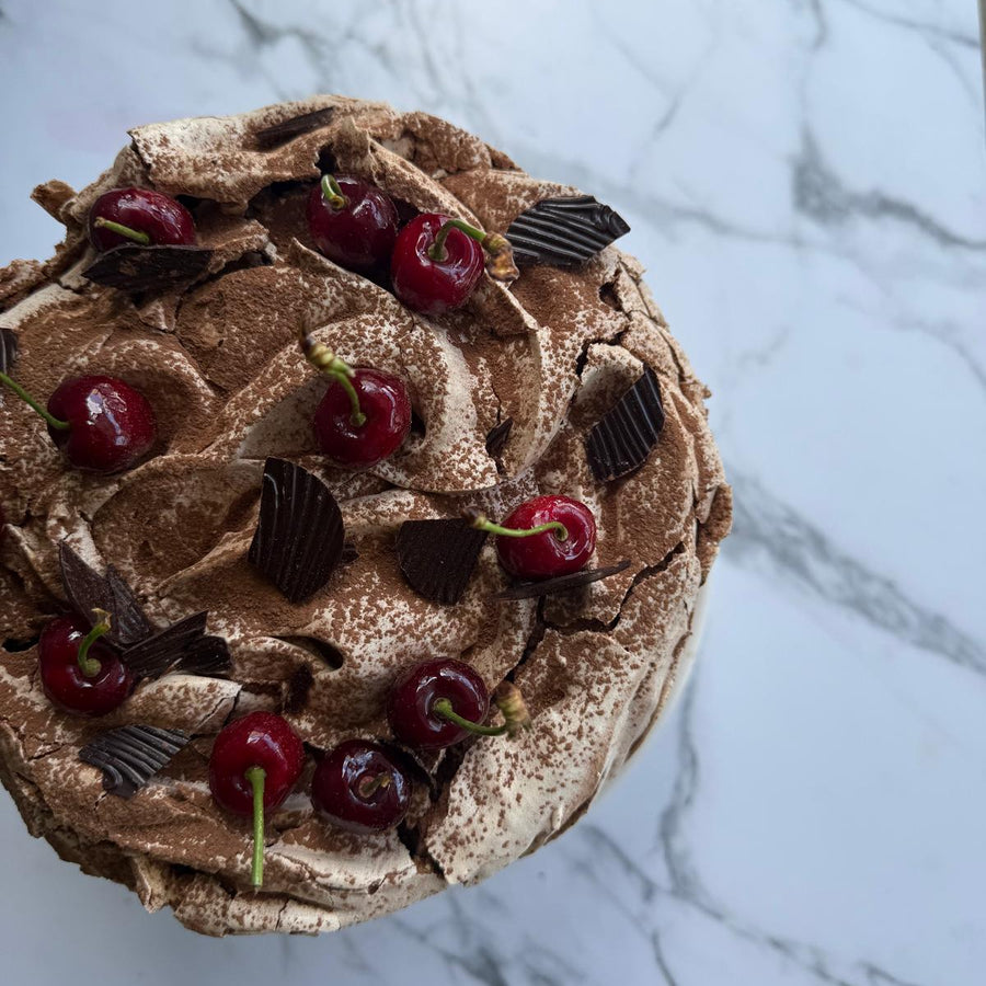 Black Forest sponge cake with swirls of chocolate meringue, cherries and tempered chocolate, sitting on a marbled surface