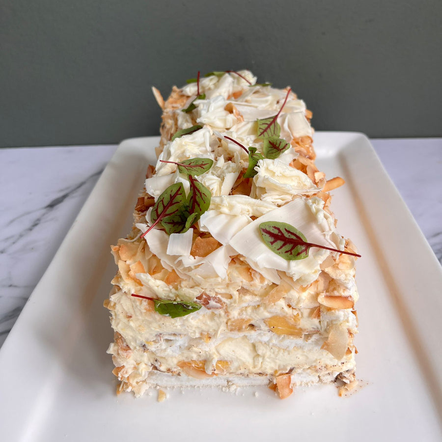 Layers of pavlova with mango and cream covered with tempered white chocolate and coconut served on a marble bench top