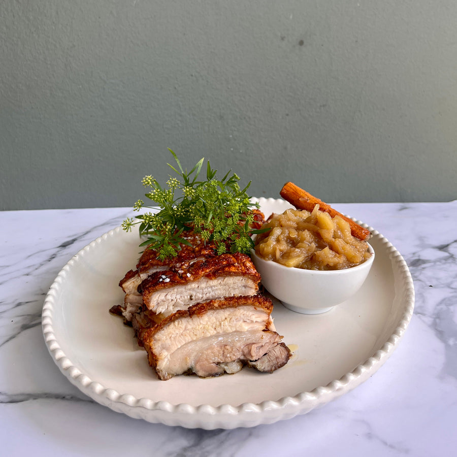 Plated dish with sliced roasted pork belly and paired with apple
chutney  on a marble surface.