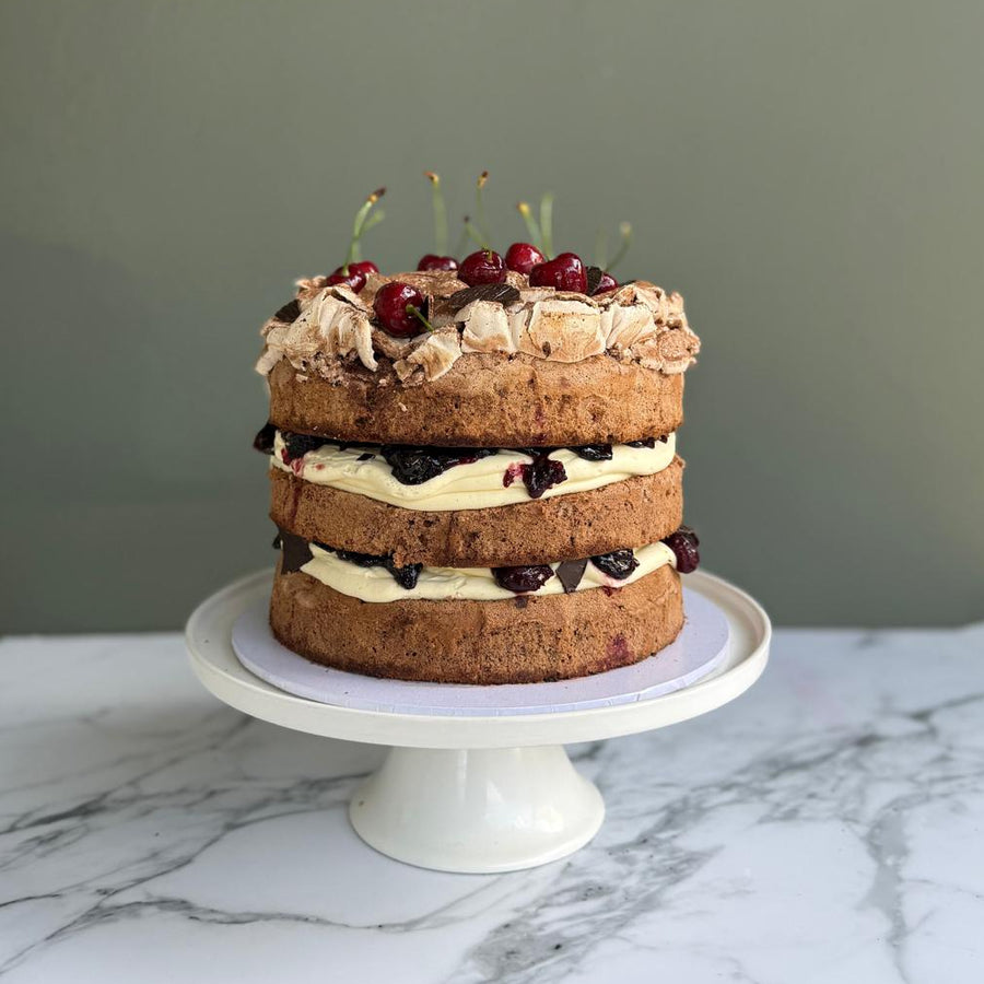 Three layered chocolate sponge, cream, cherries, chocolate on a cake stand 
