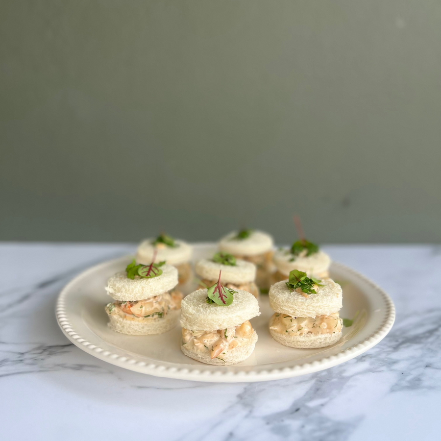 Platter of finger food with prawn cokctail sandwiches topped with a leaf of read sorrel on a marble surface