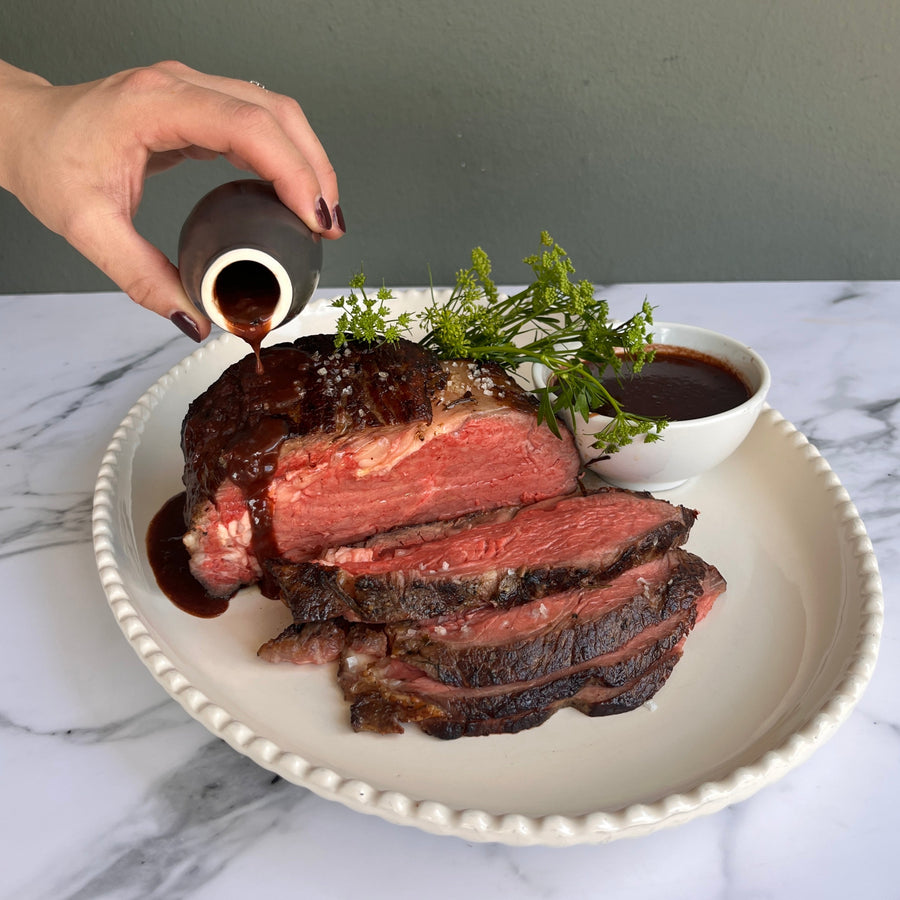 Plated sliced beef with a red wine and shallot reductions, being drizzled by a hand on a marble surface.