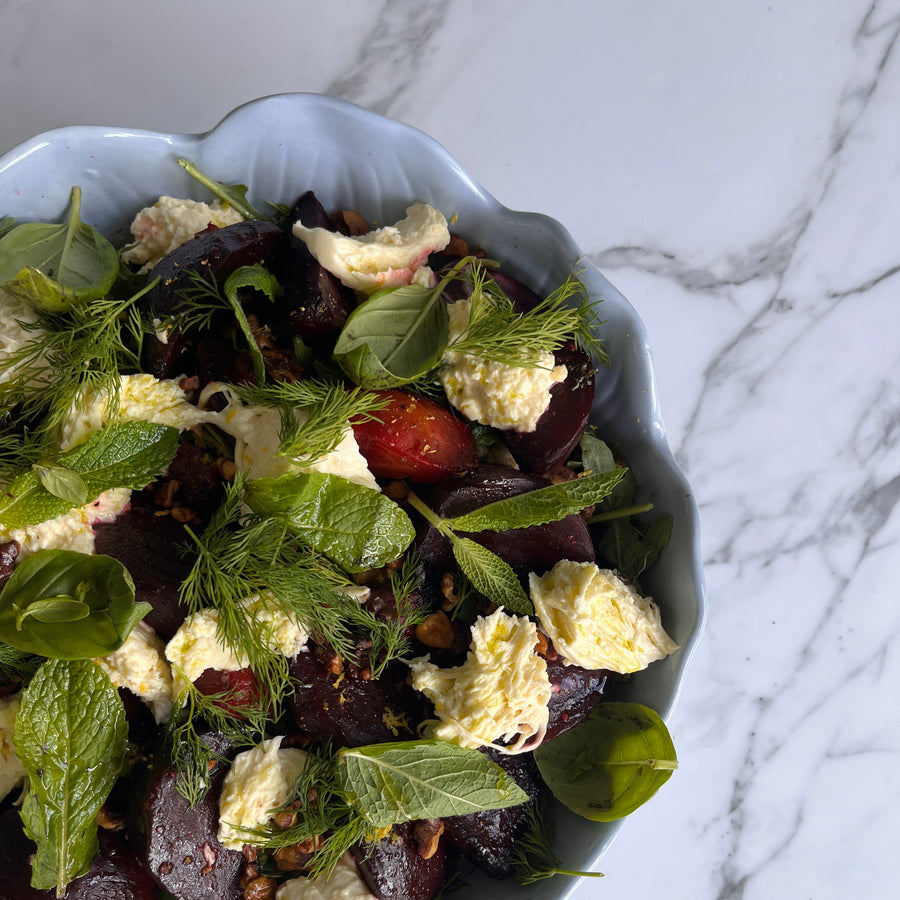 Salad with beetroot, blood oranges, spiced walnuts and stracciatella in a blue bowl on a marble surface