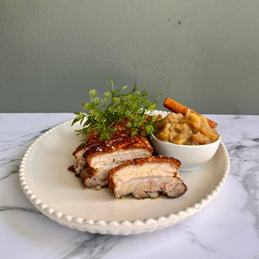 Plated dish with sliced roasted pork belly and paired with apple
chutney  on a marble surface.