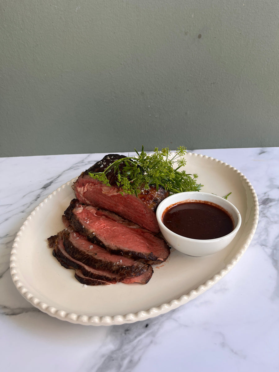 Sliced steak with accompanied by a small bowl of red wine and shallot reduction sauce.