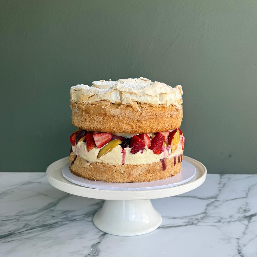 Layered sponge cake fillet with berries and market fresh peaches with berries syrup and topped with
lashings of roasted meringue on a white cake stand. 